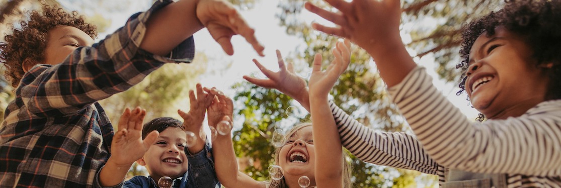 A group of children laughing playing outside with bubbles