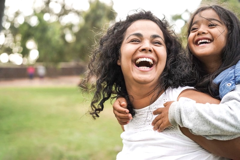 a mom giving her young daughter daughter a piggyback ride laughing